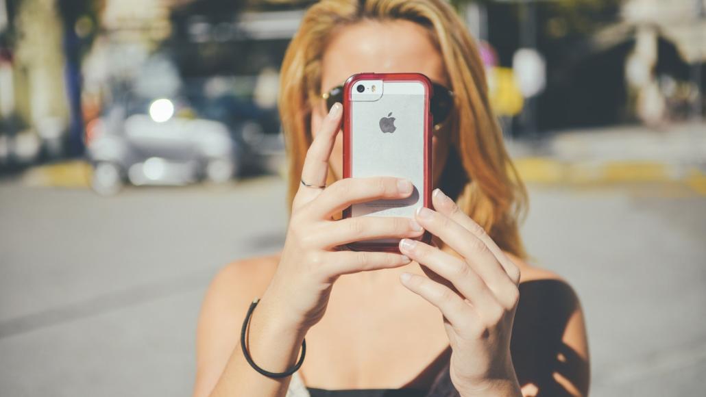 Une femme tient un téléphone portable dans la rue (© PublicDomainPictures)